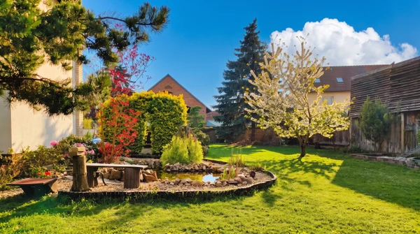 Scène extérieure d'un jardin résidentiel avec haie parfaitement taillée longeant une pelouse verte uniforme sous ciel bleu partiellement nuageux